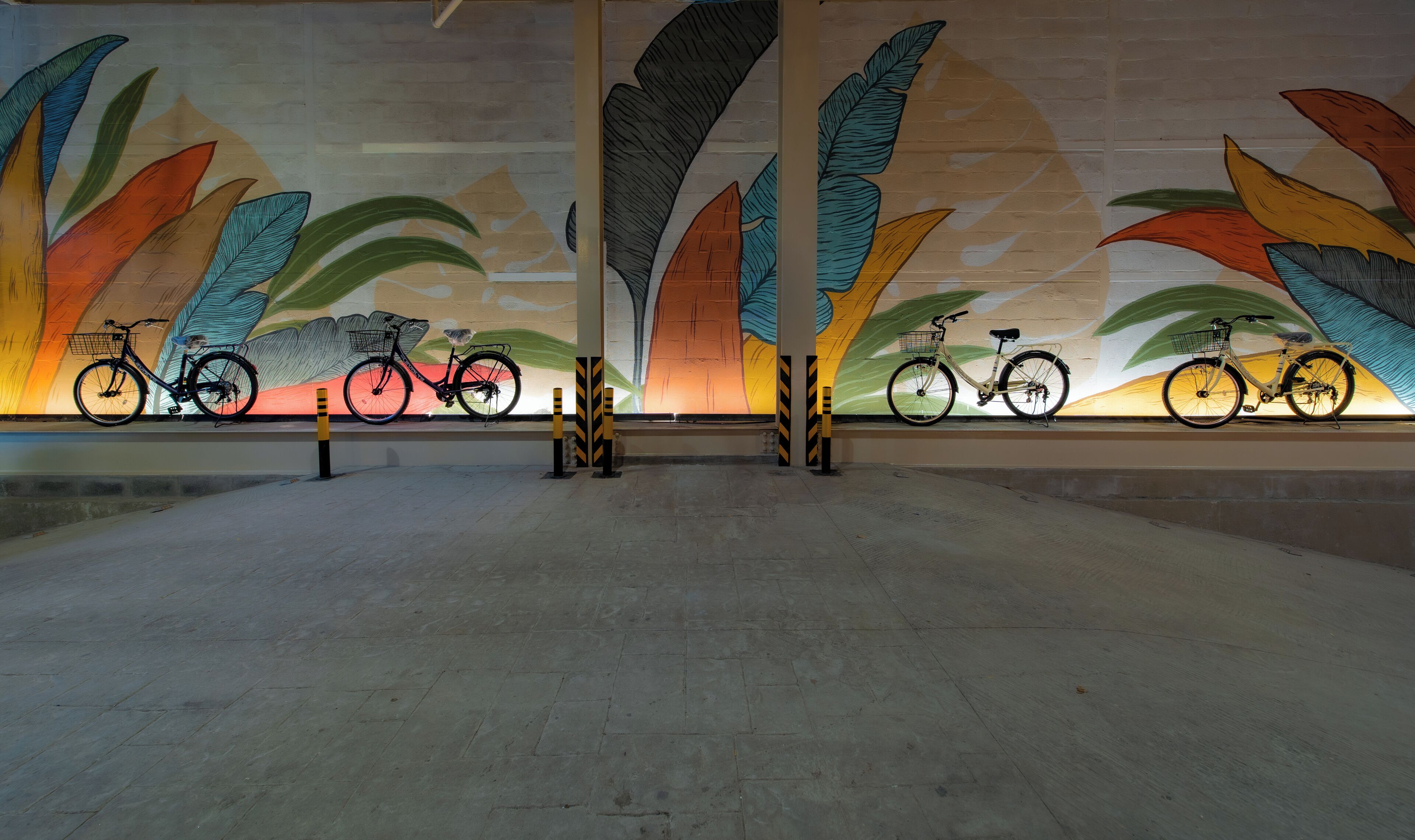 A spacious indoor area with a mural of large leaves and bicycles.