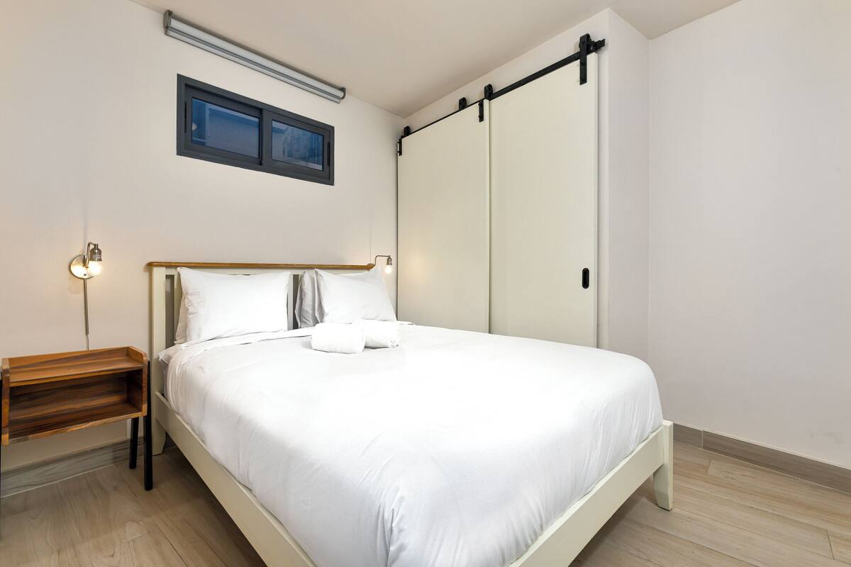 A neatly made bed with white linens, a bedside table with a lamp, and a sliding door closet.