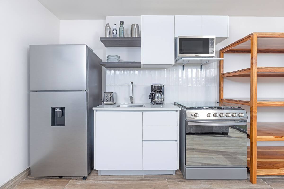 A compact kitchen with a stainless steel refrigerator, a microwave, a coffee maker, and a stove.