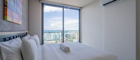 A hotel room with a large bed, a view of the city, and an air conditioning unit.