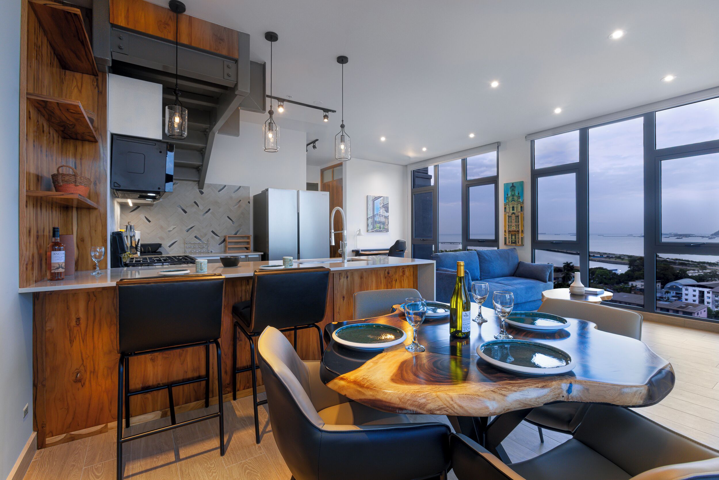 A modern kitchen with a wooden island, bar stools, and a dining table set for four.