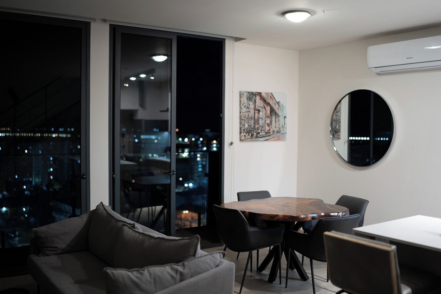 Una sala de estar moderna con vista a la ciudad, un comedor con mesa redonda y un espejo grande en la pared.