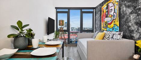 A modern living room with a sofa, dining table, and a city view through large windows.