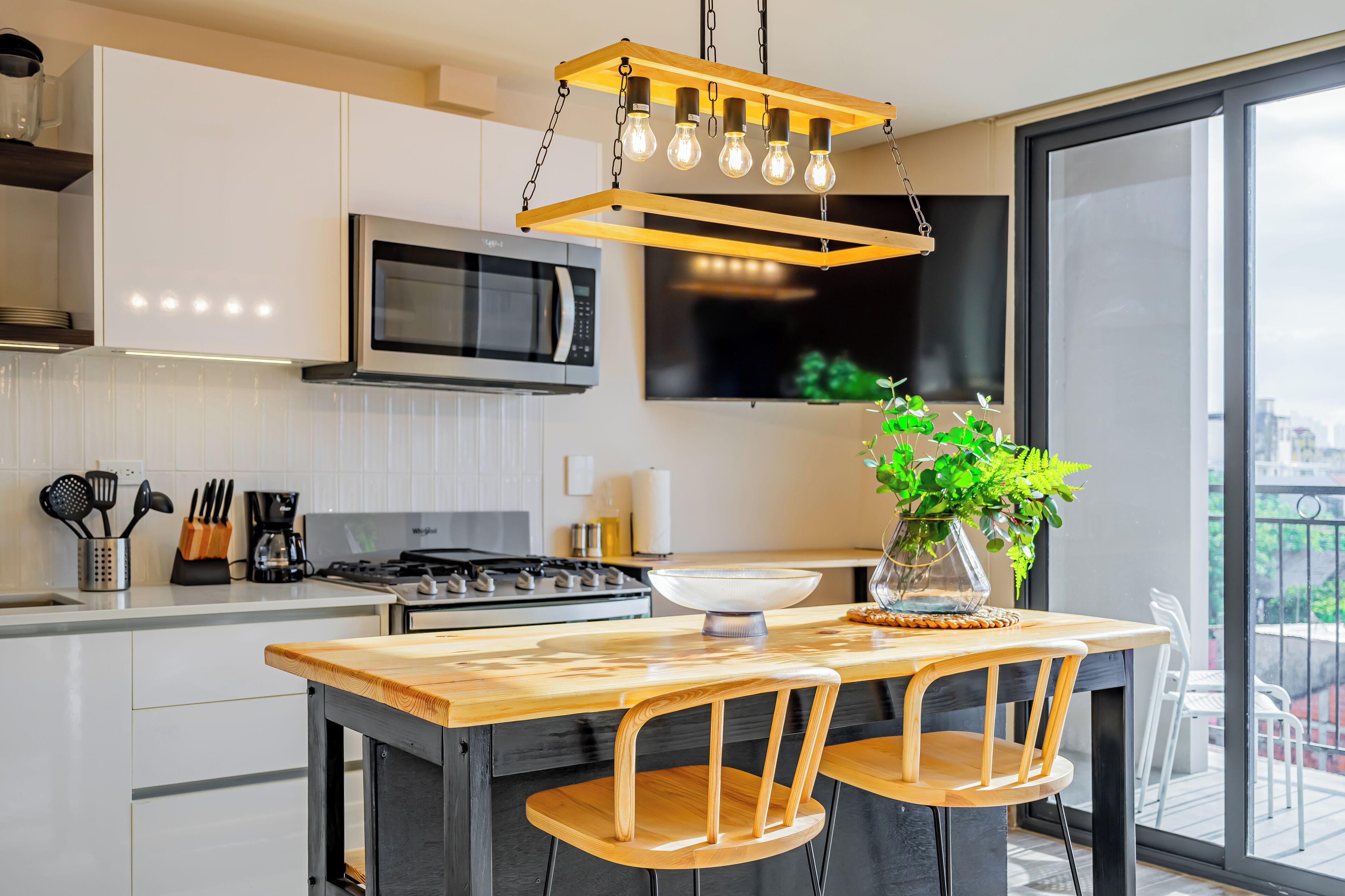 A modern kitchen with a wooden island, stainless steel appliances, and a large window offering a city view.