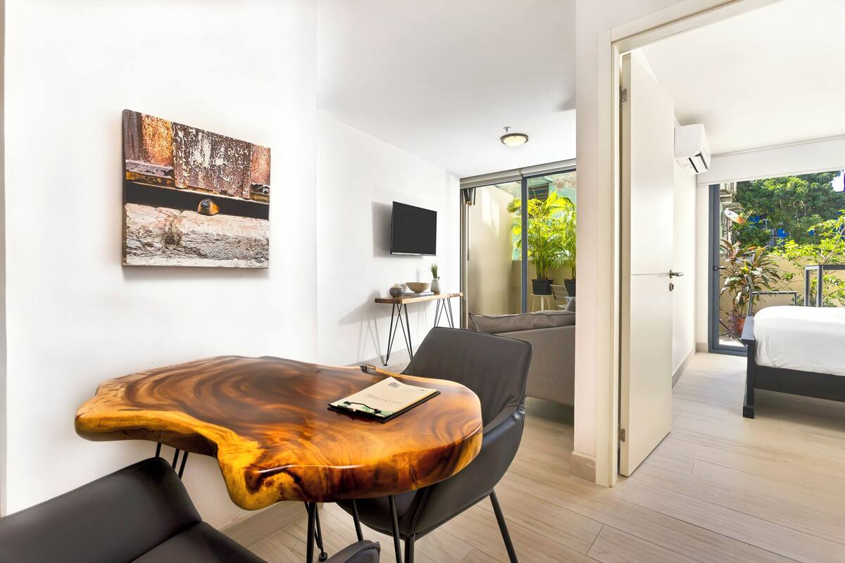 A modern room with a wooden table, a black chair, a flat-screen TV, and a painting on the wall.