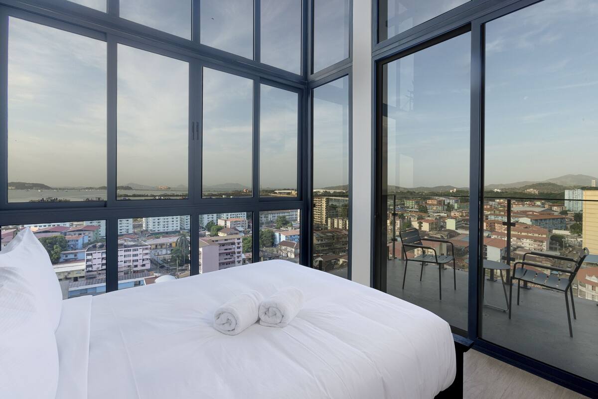 A hotel room with a large bed, two rolled towels, and a balcony with chairs.