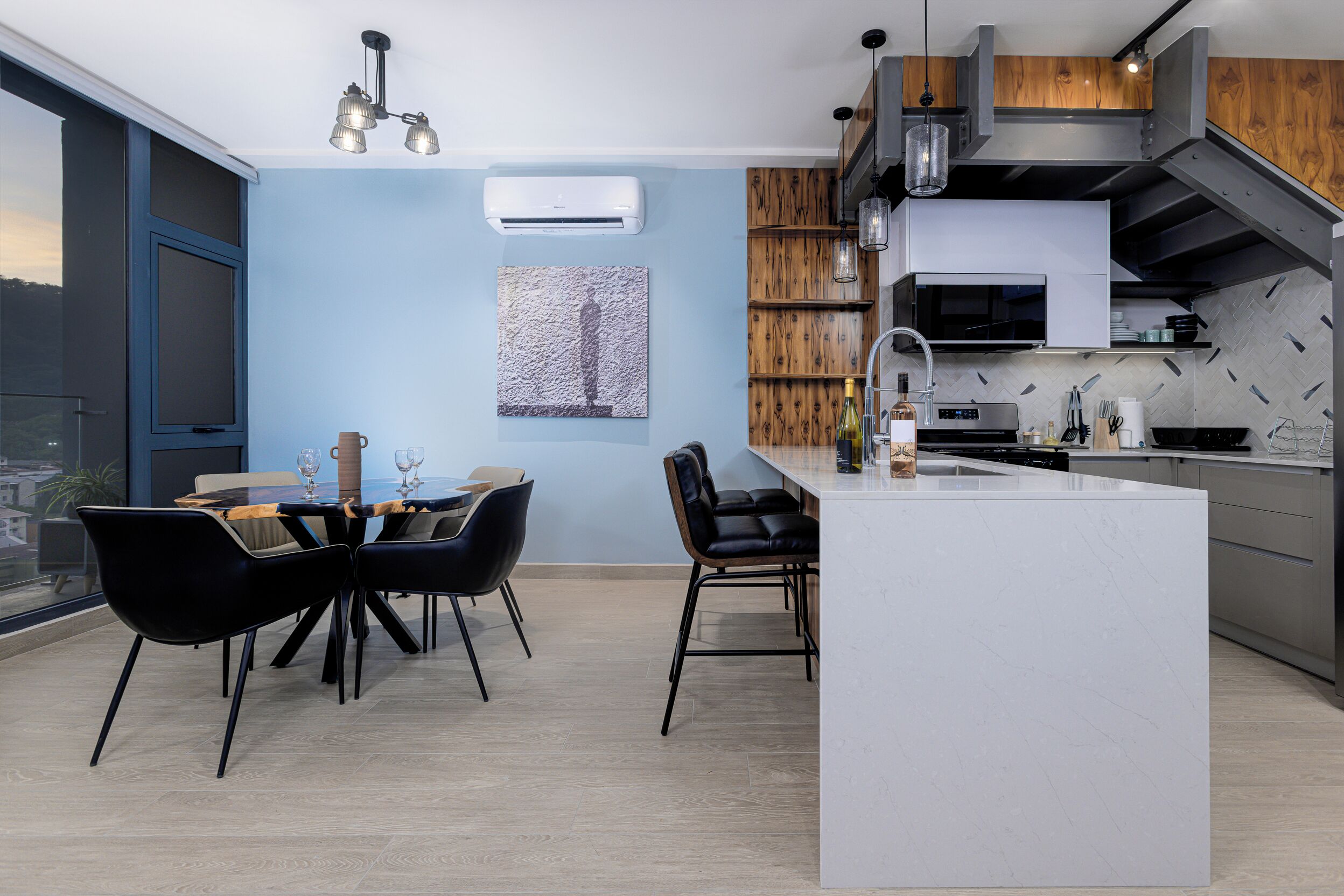 A modern kitchen with a central island, built-in appliances, and a dining area with black chairs and a table.