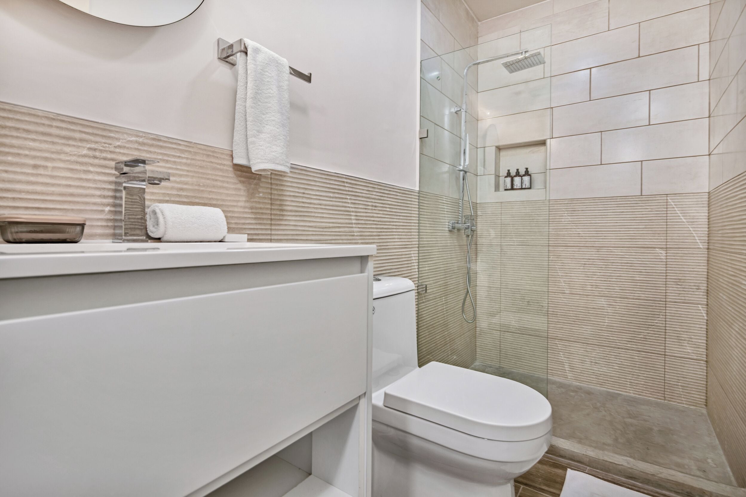 Un baño moderno con ducha de vidrio, inodoro blanco y pared cubierta de azulejos color beige.