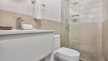 Un baño moderno con ducha de vidrio, inodoro blanco y pared cubierta de azulejos color beige.