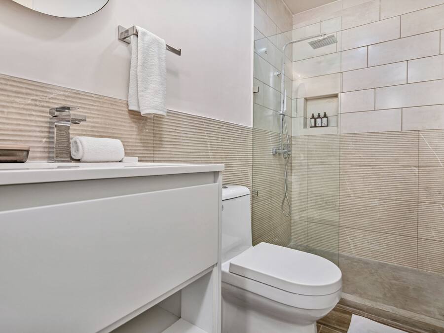 Un baño moderno con ducha de vidrio, inodoro blanco y pared cubierta de azulejos color beige.