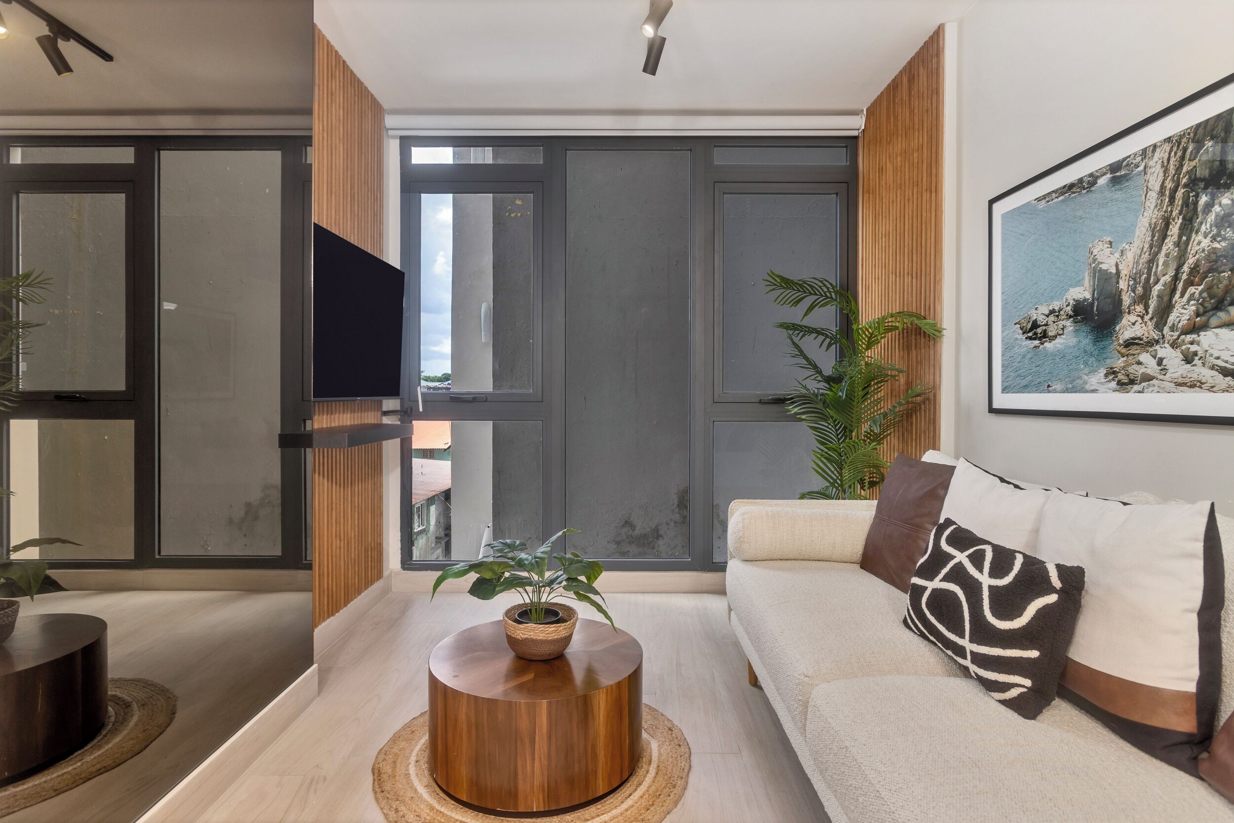 Un salón moderno con una mesa de centro de madera, un sofá con cojines estampados y un ventanal con vistas al exterior.