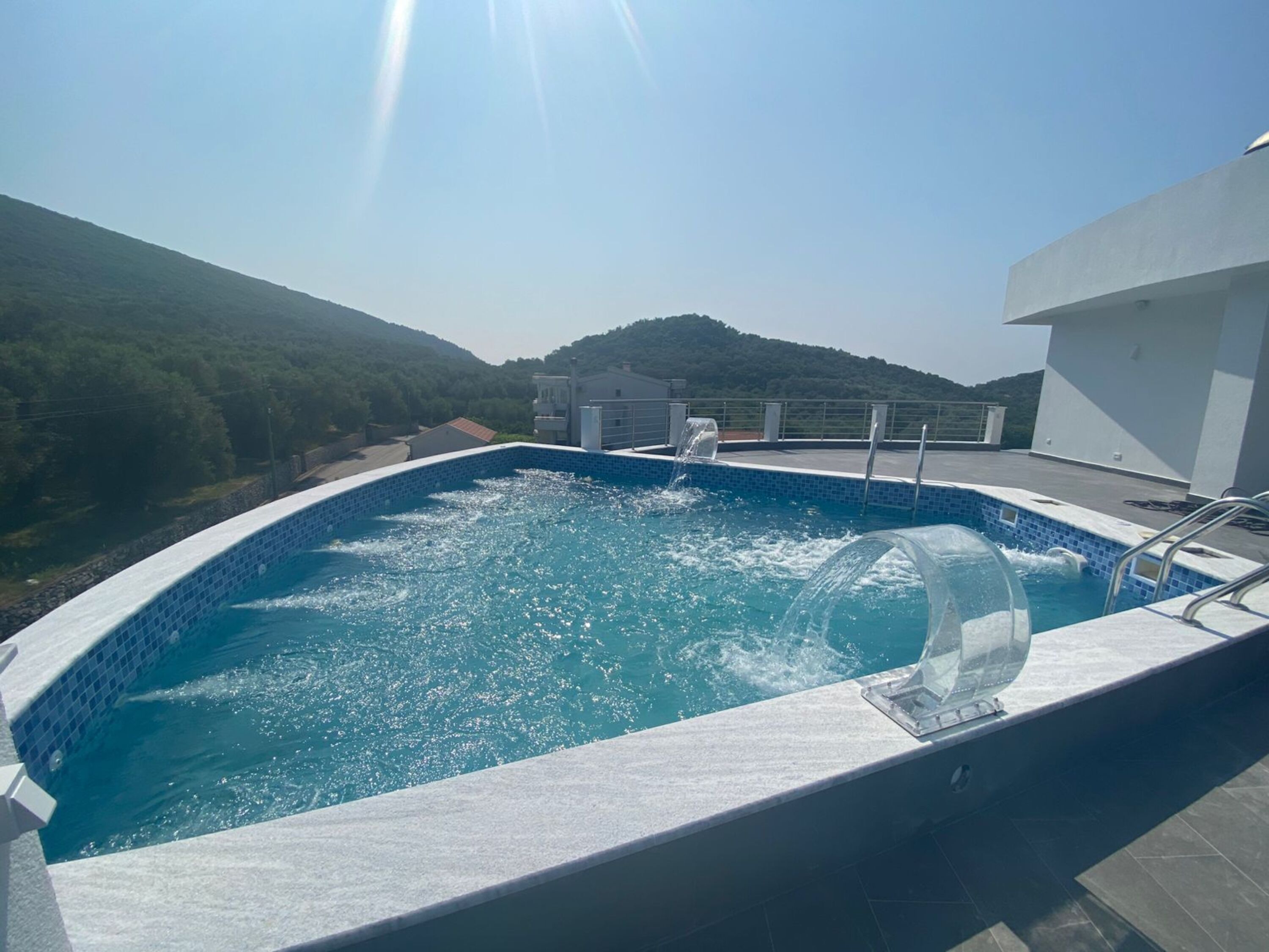 A rooftop swimming pool with clear blue water, surrounded by a white pool deck and a metal railing.