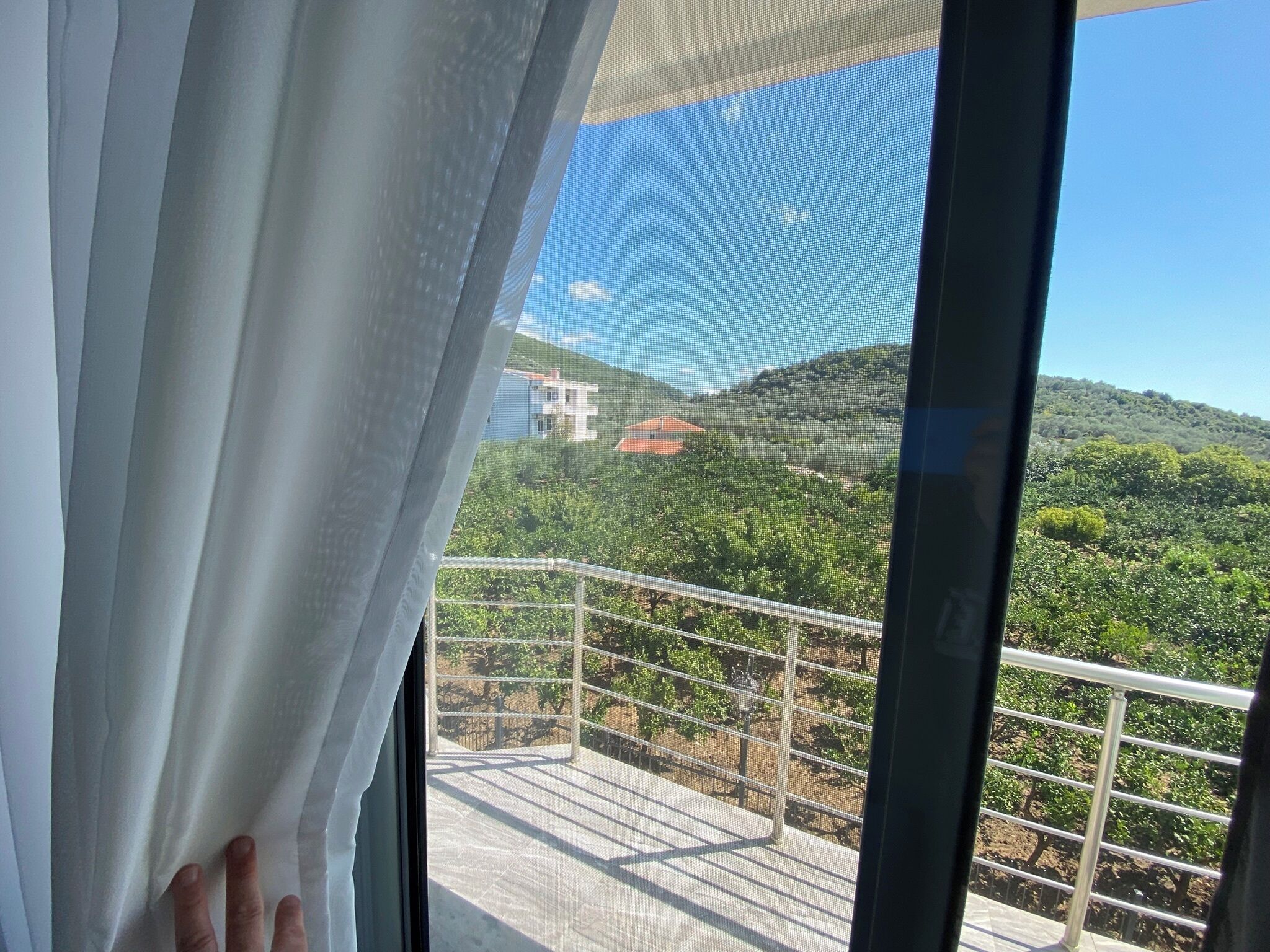 A balcony with a metal railing overlooking a vineyard and a building in the distance.