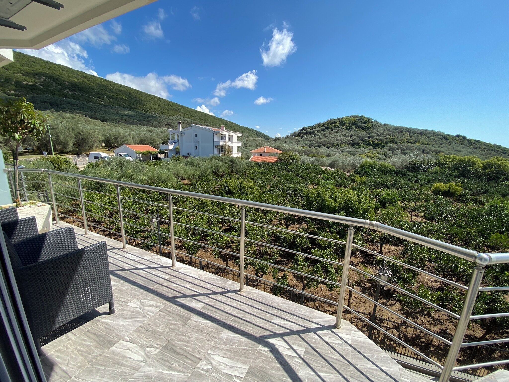 A terrace with a metal railing, a view of a vineyard, and buildings in the background.