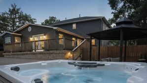 A hot tub in a backyard with a wooden deck, a covered patio, and a house with a porch. - Lake Hamilton Carriage House, 5 bed, 3.5 bath, Sleeps 17, Game rm, pet friendly! (Hot Springs)