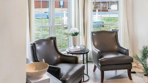 A room with two leather armchairs, a small table with a vase and a book, and a view of a residential area through large windows. - Lake Hamilton Carriage House, 5 bed, 3.5 bath, Sleeps 17, Game rm, pet friendly! (Hot Springs)