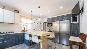 A modern kitchen with a central island, stainless steel appliances, and a dining area with bar stools. - Villa Can Truyet - Four Bedroom Villa, Sleeps 7 (Santa Eulària des Riu)