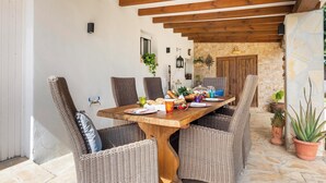 A dining area with a wooden table and wicker chairs, stone walls, and a stone floor. - Villa Can Truyet - Four Bedroom Villa, Sleeps 7 (Santa Eulària des Riu)
