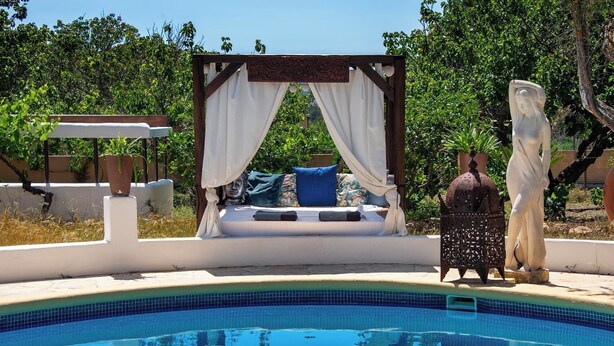 A poolside relaxation area with a bed, a statue, and a pergola with drapes. - Villa Can Truyet - Four Bedroom Villa, Sleeps 7 (Santa Eulària des Riu)