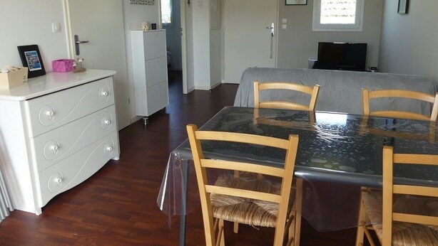 Un comedor con mesa de vidrio y sillas de madera, un aparador blanco con cajones y una puerta que da a otra habitación.