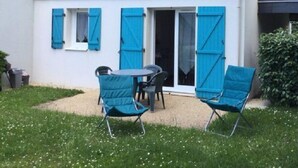 Una casita con techo de tejas, un patio con mesa y sillas, y una puerta corrediza de vidrio.