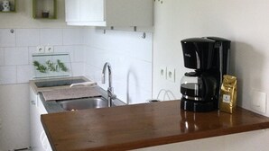 Una pequeña cocina con armarios blancos, una encimera de madera, una cafetera y un paquete de café.