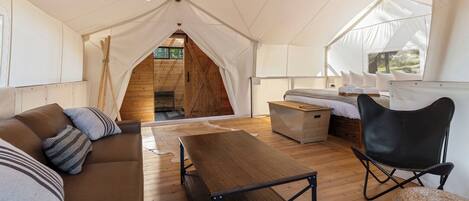A tented accommodation with a wooden interior, a sofa, a table, and a chair.
