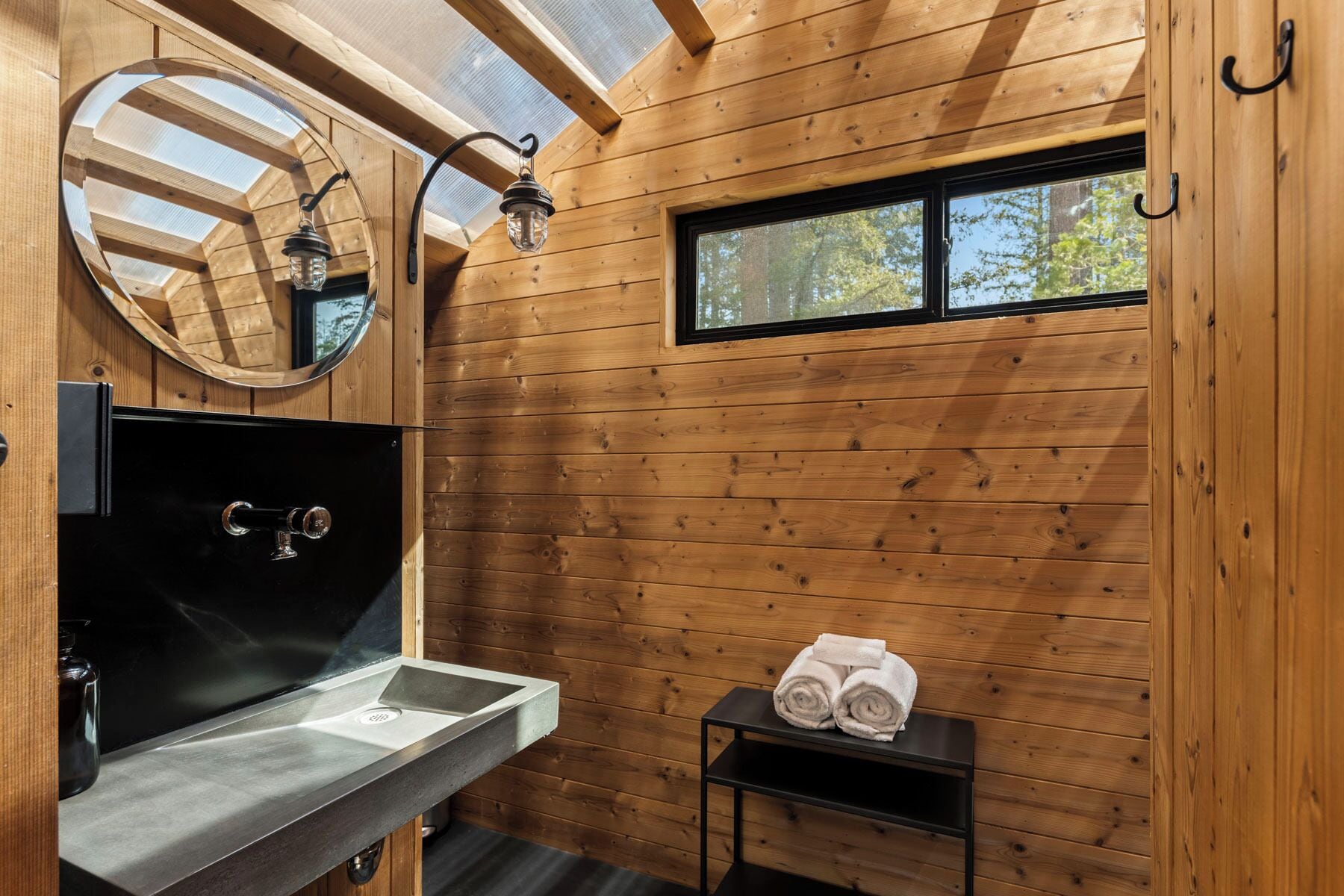 Une salle de bain rustique, aménagée dans une cabane en bois, avec un lavabo, un miroir et une fenêtre.
