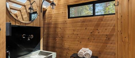 Une salle de bain rustique, aménagée dans une cabane en bois, avec un lavabo, un miroir et une fenêtre.
