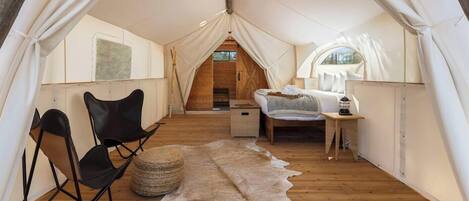 A tented accommodation with a bed, a chair, a small table, and a cowhide rug.