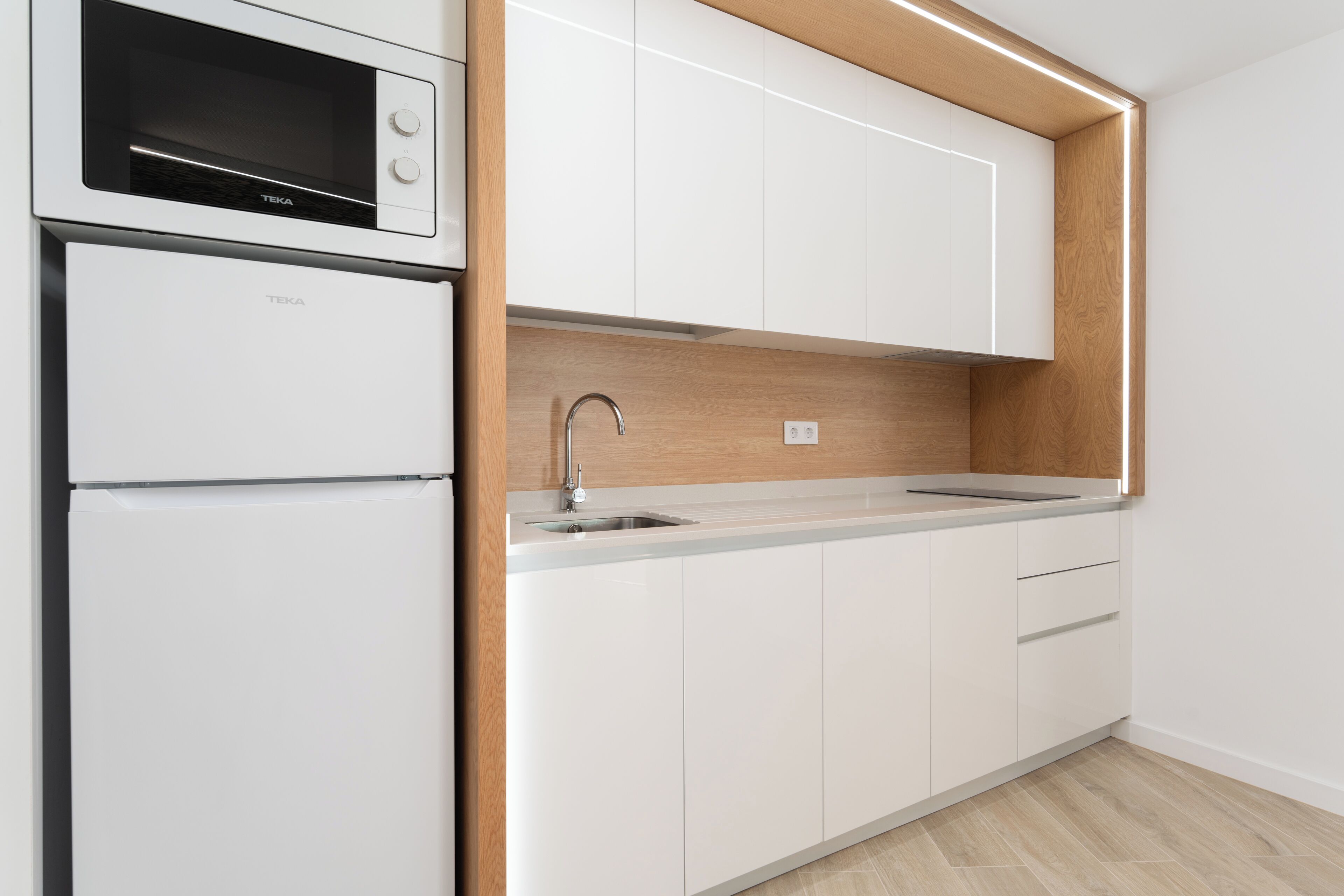 Una cucina moderna con mobili bianchi, forno integrato e una parete decorata in legno.