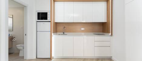Una cocina compacta con gabinetes blancos, un microondas y un lavamanos.