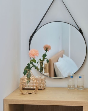 A round mirror with a black frame, a wooden bedside table, a wicker basket with a plant, and two clear glass bottles. - HONEYMOON HOTEL 2 (Hanoi)