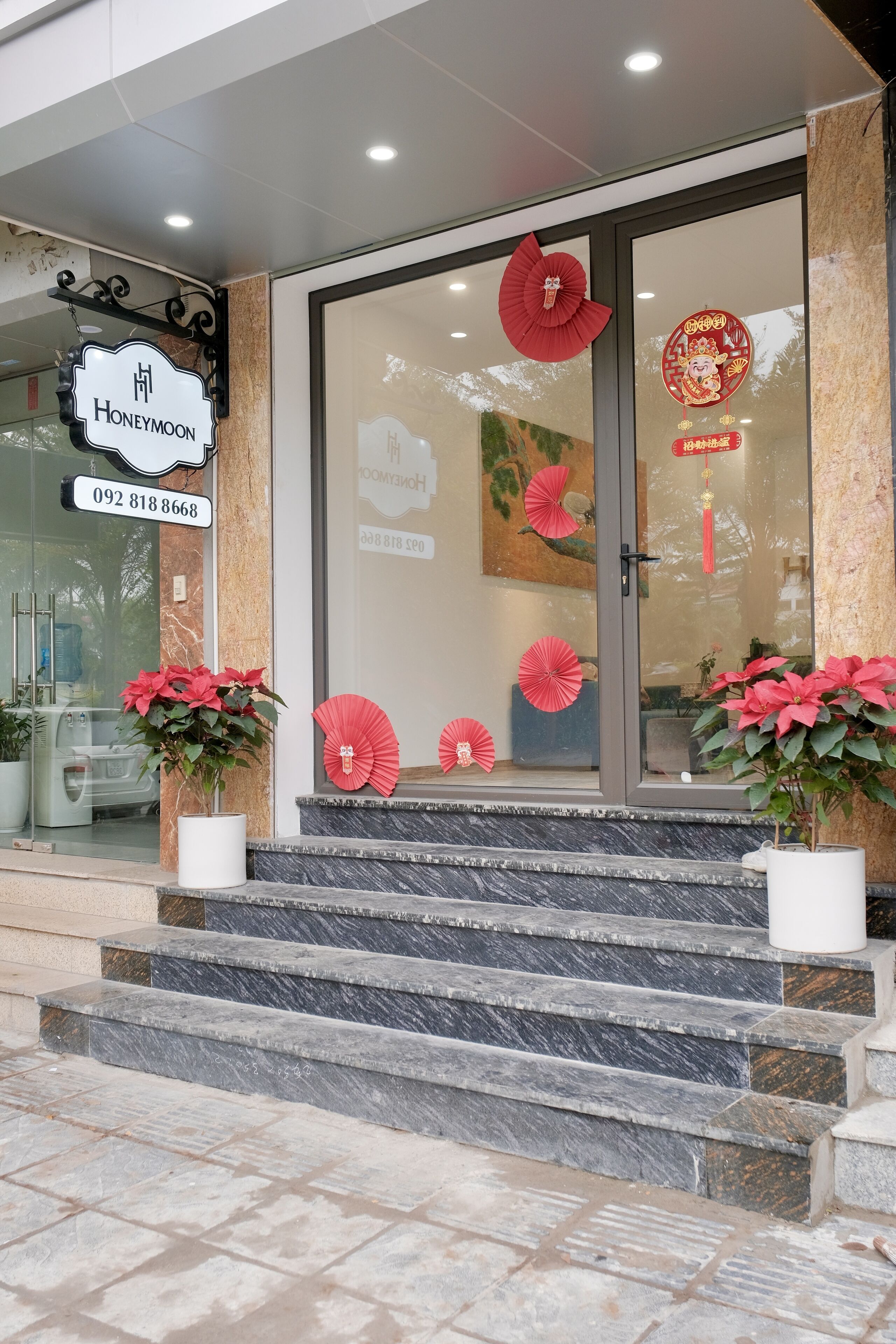 A hotel entrance with a sign reading "Honeymoon," a phone number, and decorative red fans and plants.