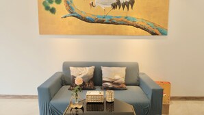 A living room with a blue sofa, two decorative pillows, a vase with flowers, and a coffee table with a vase and a box. - HONEYMOON HOTEL 2 (Hanoi)
