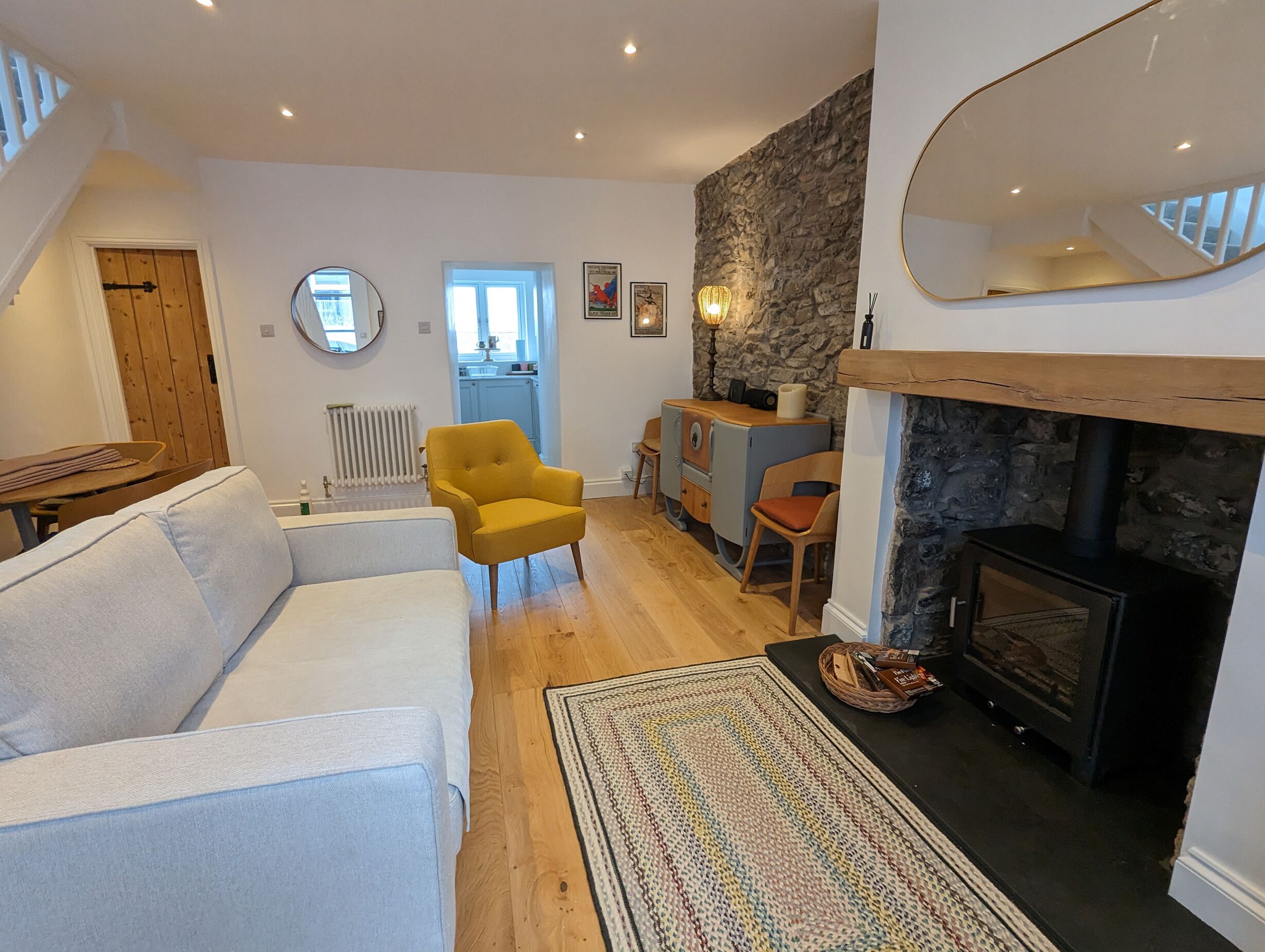 A living room with a fireplace, a yellow armchair, a white sofa, and a kitchen in the background.