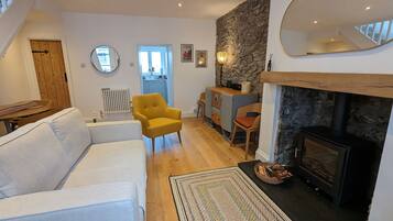 A living room with a fireplace, a yellow armchair, a white sofa, and a kitchen in the background.