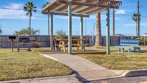 A wooden gazebo with a picnic table and benches, surrounded by a grassy area and a wooden fence. - Lighthouse at the beach (Corpus Christi)