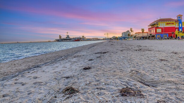 A beach with a large ship, colorful buildings, and a clear sky. - Lighthouse at the beach (Corpus Christi)