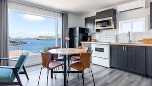 A modern kitchen with a view of the sea, a dining area with chairs, and a large window. - Cliffs Edge Retreat (Tors Cove)