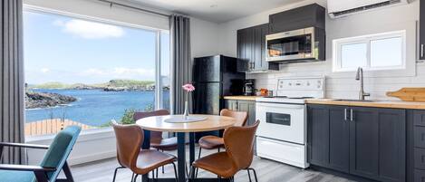 A modern kitchen with a view of the sea, a dining area with chairs, and a large window.