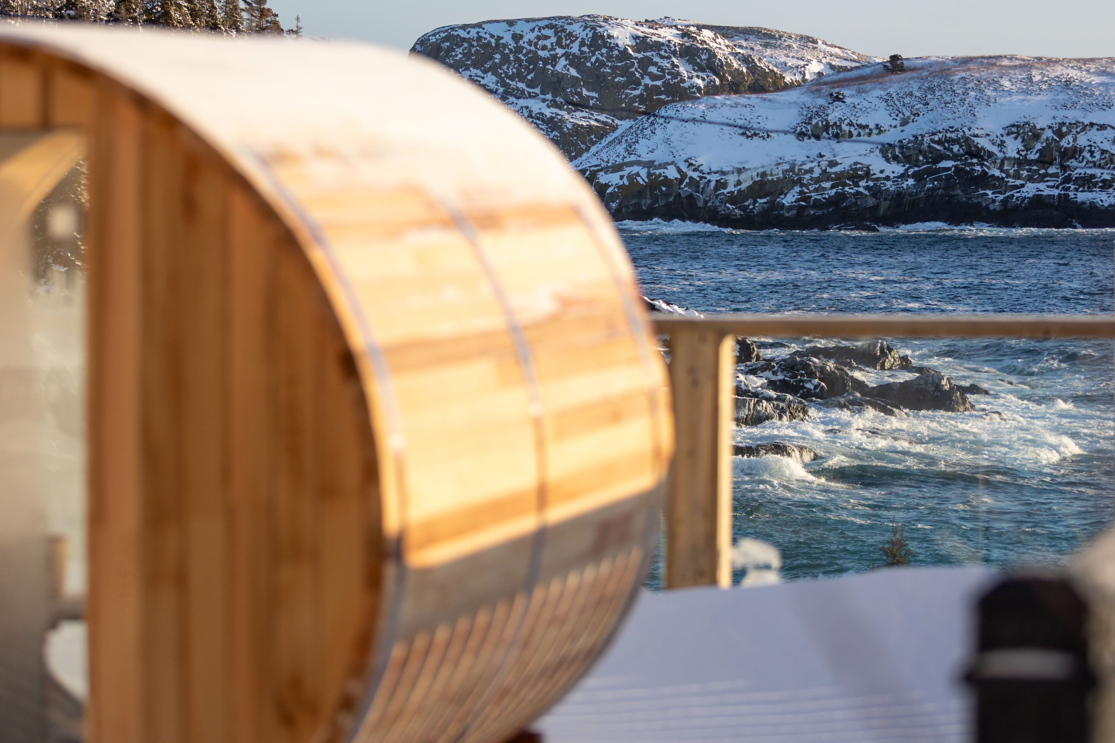 Una botte di legno, una ringhiera e un litorale roccioso con neve.