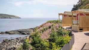 A coastal wooden cabin with a view of the sea and rocky shoreline. - Cliffs Edge Retreat (Tors Cove)
