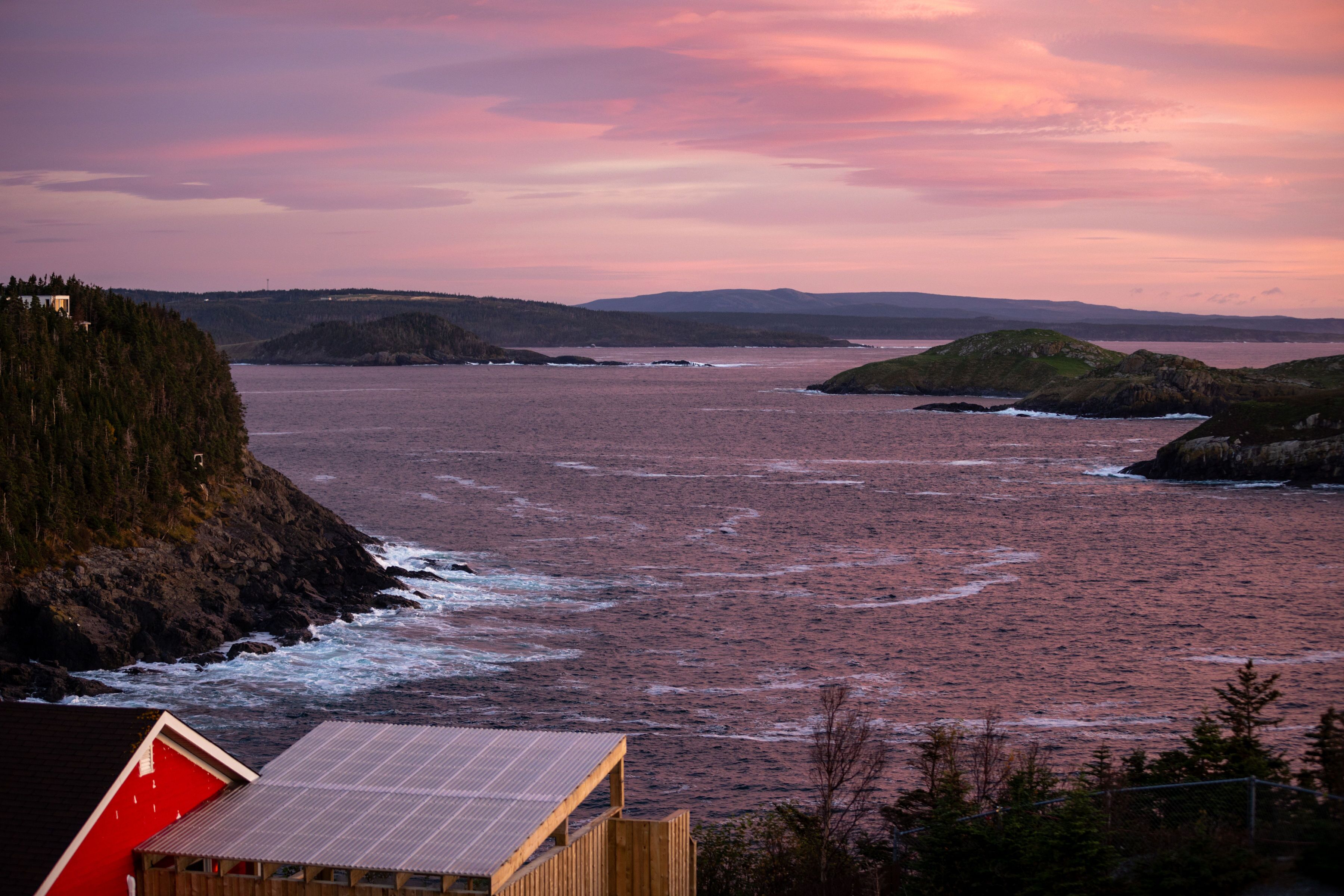 Une vue sur la côte, avec un bâtiment en bois et une structure rouge, probablement une cabane ou un chalet, dominant la mer.