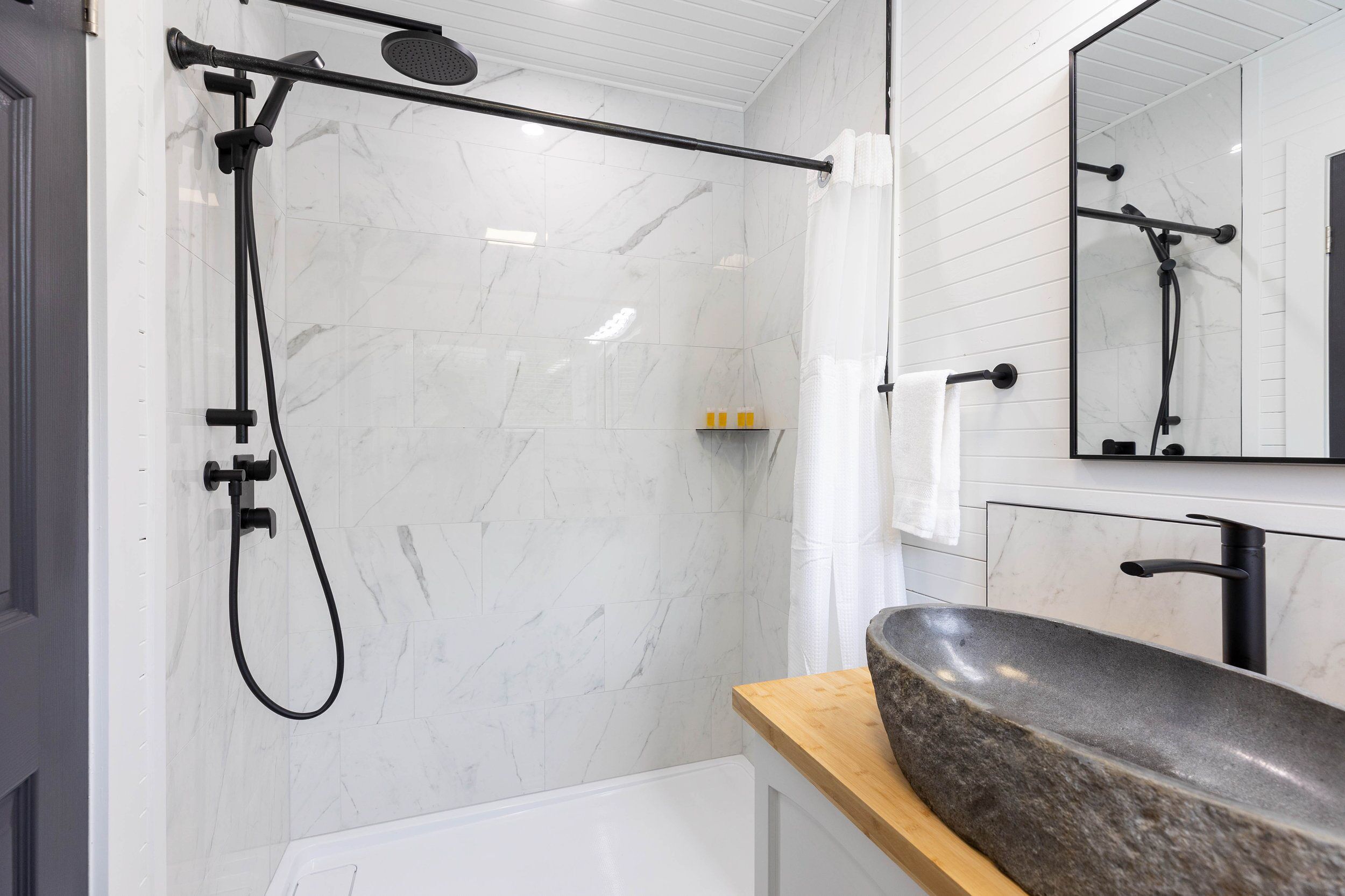 Ein modernes Badezimmer mit Dusche, Waschbecken mit Steinbecken und Spiegel über dem Waschbecken.