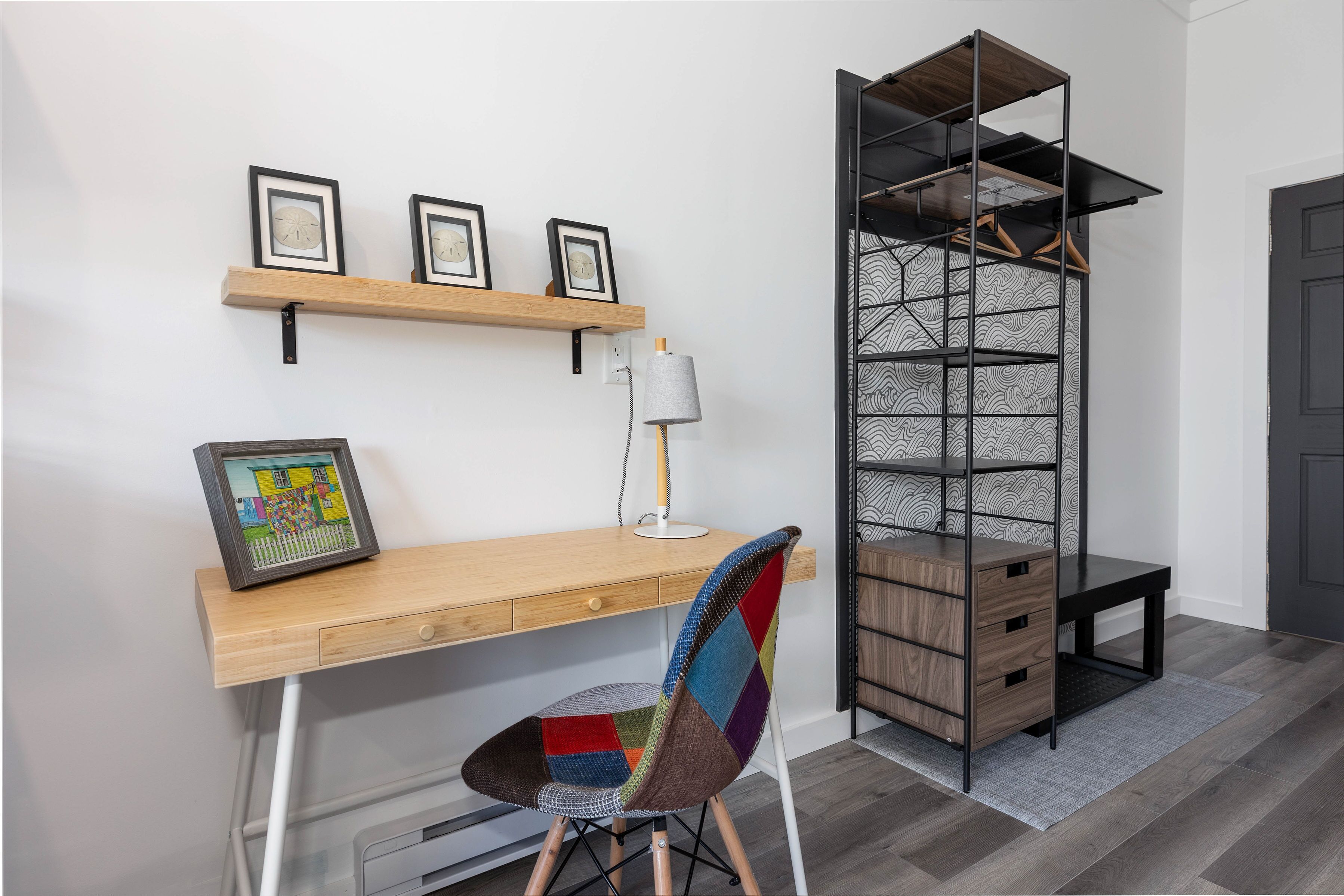 A modern workspace with a wooden desk, a colorful chair, a lamp, and a black shelving unit.