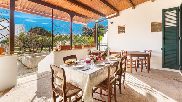 An outdoor dining area with a table set for four, surrounded by wooden chairs, under a wooden pergola with a view of greenery and a clear sky. - Villa Donna Linda by BarbarHouse (Taviano)
