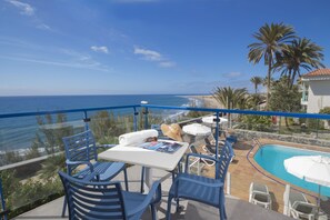 A balcony with a pool, chairs, and a table overlooking the ocean. - Alsol Los Caribes 1 (San Bartolomé de Tirajana)
