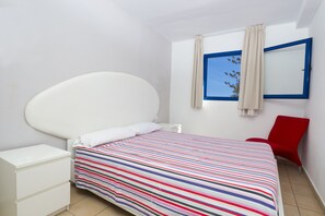 A bedroom with a bed, a nightstand, a red chair, a window with curtains, and a mirror on the wall. - Alsol Los Caribes 1 (San Bartolomé de Tirajana)