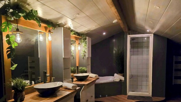 Uma casa de banho moderna com soalho de madeira, um espelho grande, duas bacias e zona de duche.
